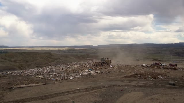 Aerial drone point of view of a commercial landfill garbage dump with tractors scraping the trash