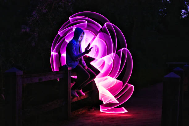 Boy sitting on a bridge with his smartphone in his hand Violet light effect with a light saber in lightpainting long exposure photos stock pictures, royalty-free photos & images