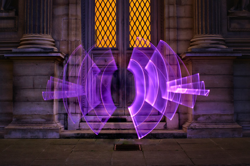 Abstract shape made with a bright lightsaber in front of an illuminated window door of an old building