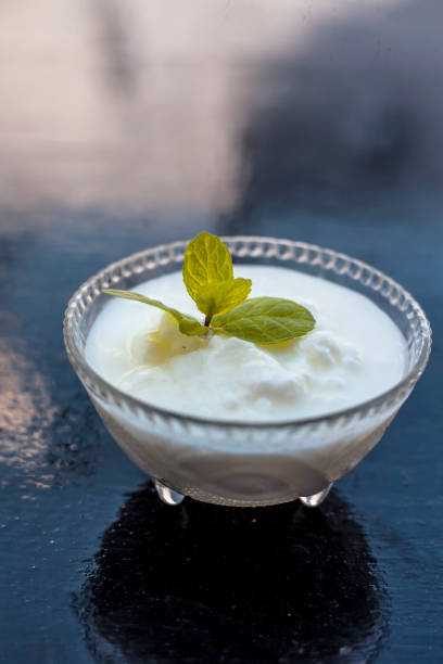 Close up of raw organic curd in a glass bowl along with mint leaf on the top for decoration on wooden surface. Close up of raw organic curd in a glass bowl along with mint leaf on the top for decoration on wooden surface. curd cheese photos stock pictures, royalty-free photos & images