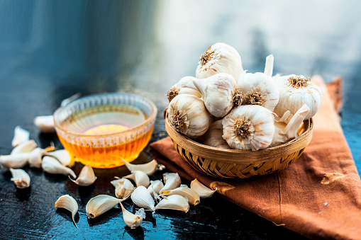 Raw garlic and honey with separate bowl on wooden surface used together for the treatment of lower high cholesterol and blood pressure and many more.