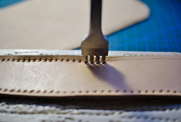 Leather working four prong chisel hole punch close up. Punching holes for stiching with metal tool. Selective focus.