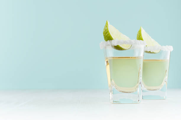 hausgemachte sommerschussgetränke tequila mit scheibenkalk, das salz der felge in schuss glas auf weichem hellem pastellblau. - tequila shot tequila salt lemon stock-fotos und bilder