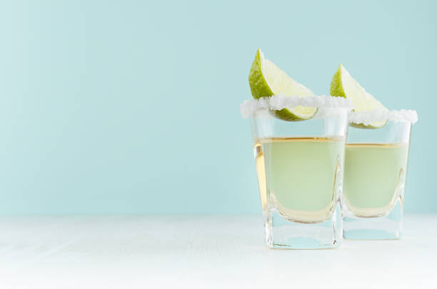 homemade summer shot drink tequila  with slice lime, salt of rim in  shot glass on soft light pastel blue background. - tequila shot imagens e fotografias de stock