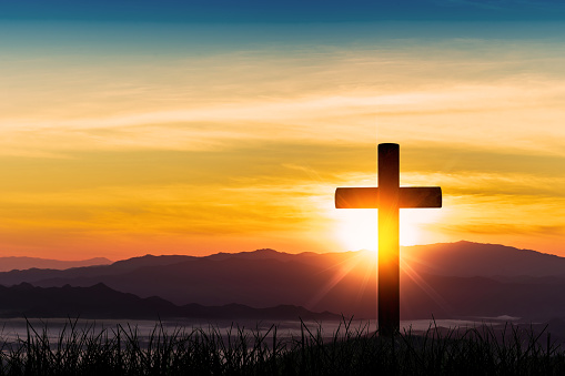 Silhouette of cross on mountain sunset background.