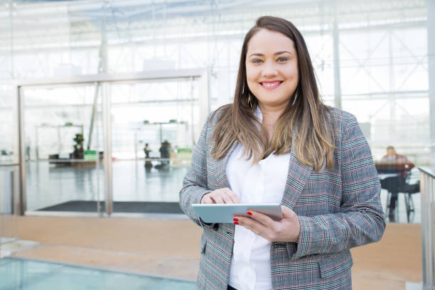 dame positive avec la tablette posant dans le centre d’affaires - heavy work photos et images de collection