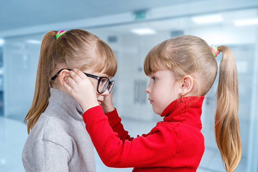 A child puts glasses on his twin sister on a blurred background.