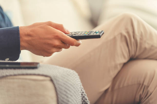 Man sitting on the sofa watching television. He is holding a tv remote control.