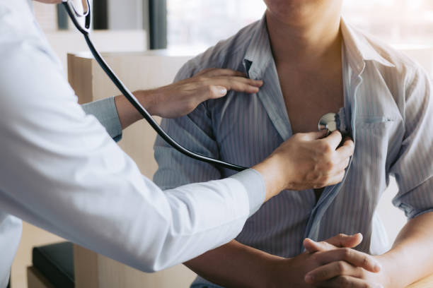 o doutor asiático está usando um estetoscópio escuta o batimento cardíaco do paciente idoso. - physical checkup - fotografias e filmes do acervo