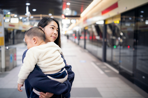 Asian mother carrying her sleeping baby and waiting for a train.