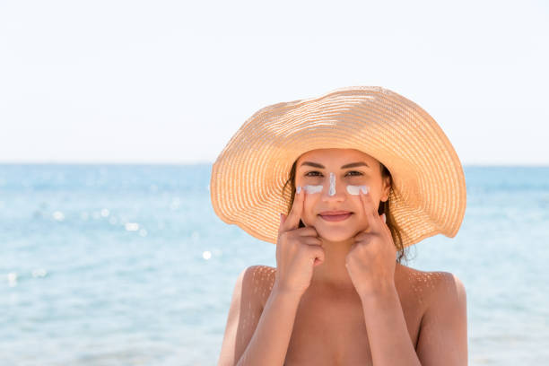 bella donna protegge la sua pelle sul viso con crema solare in spiaggia - sun protection foto e immagini stock