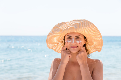 Pretty woman protects her skin on face with sunblock at the beach.