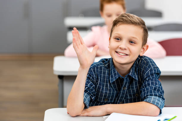 istock Schoolboy in checkered shirt raising hand up during lesson in classroom 1149728727