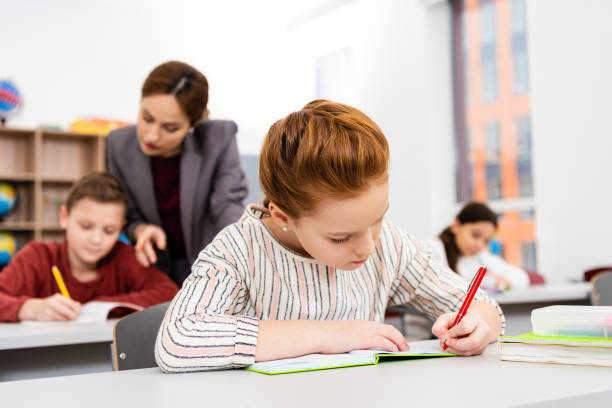 istock Cute ginger schoolgirl writing in notebook during lesson in classroom 1149728980