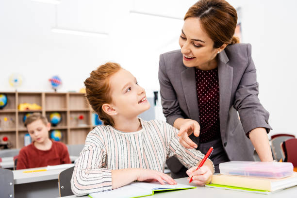 istock Teacher standing near desk and explaining lesson to pupil in classroom 1149728981