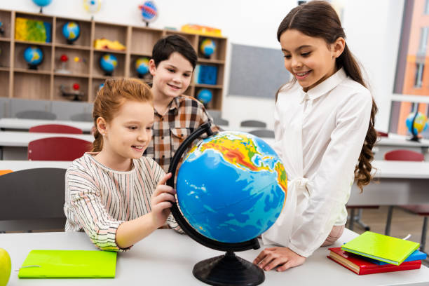 istock Three cheerful pupils playing with globe in classroom during geography lesson 1149729063