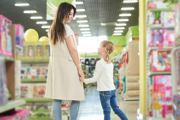 Happy mother and girl walking in shopping centre, toy shop. Happy mother brunette and little girl walking, posing in toy store of shopping centre. Big modern department store with many shelves and colorful box with toys. toy store stock pictures, royalty-free photos & images