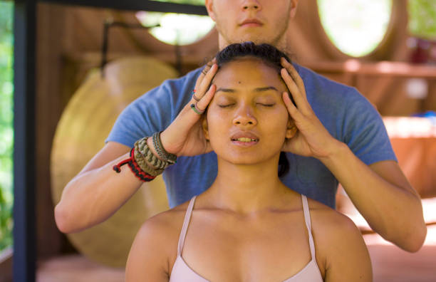 natural lifestyle portrait of young beautiful and relaxed asian balinese woman receiving a healing facial and head thai massage by male therapist at traditional spa in beauty wellness concept - bali male beautiful ethnicity imagens e fotografias de stock