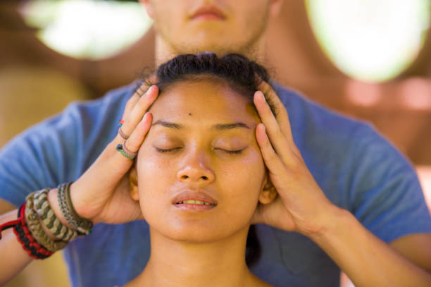 natural lifestyle portrait of young beautiful and relaxed asian balinese woman receiving a healing facial and head thai massage by male therapist at traditional spa in beauty wellness concept - bali male beautiful ethnicity imagens e fotografias de stock