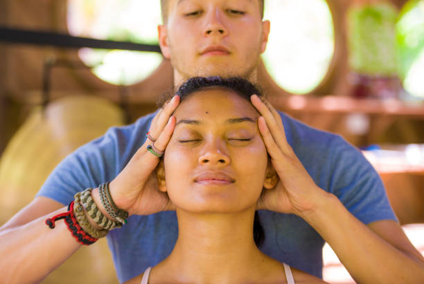 natural lifestyle portrait of young beautiful and relaxed asian balinese woman receiving a healing facial and head thai massage by male therapist at traditional spa in beauty wellness concept - bali male beautiful ethnicity imagens e fotografias de stock