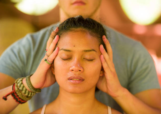 naturisches lifestyle-porträt von jungen schönen und entspannten asiatischen balinesen, die eine heilende gesichts-und kopfthail-massage von männlichen therapeuten im traditionellen spa in beauty-wellness-konzept erhalten - bali male beautiful ethnicity stock-fotos und bilder