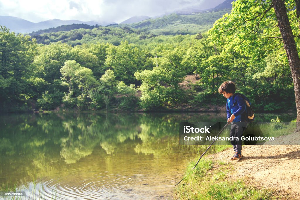 Child play fishing near lake. Little kid play with stick looks like rod and fishing on the lake in the forest on a sunny day. Child Stock Photo