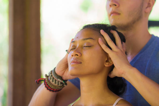 natural lifestyle portrait of young beautiful and relaxed asian balinese woman receiving a healing facial and head thai massage by male therapist at traditional spa in beauty wellness concept - bali male beautiful ethnicity imagens e fotografias de stock