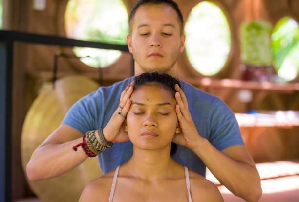 natural lifestyle portrait of young beautiful and relaxed asian balinese woman receiving a healing facial and head thai massage by male therapist at traditional spa in beauty wellness concept - bali male beautiful ethnicity imagens e fotografias de stock