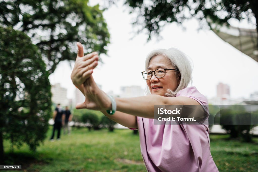 Taiwanese Lady Staying Fit With Tai Chi At The Park A senior Taiwanese lady staying fit and healthy with some Tai Chi at the park. Tai Chi Stock Photo