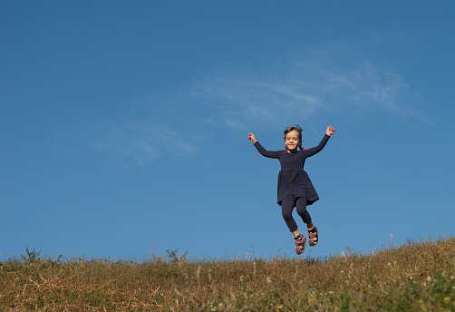 Little four years old girl in blue dotted dress jumping under blue sky. Happy smiling small child playing outdoor. Concept - happy lifestyle.