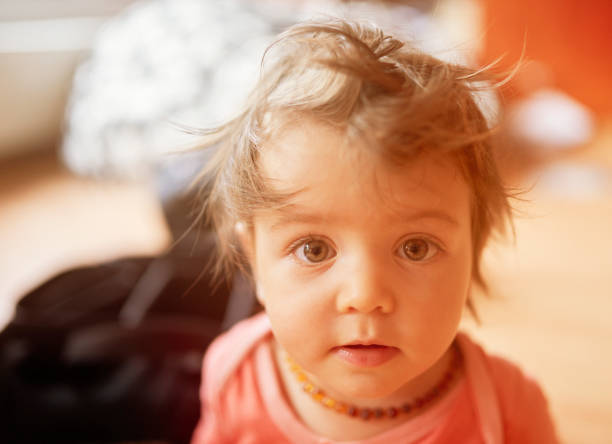 portrait of cute baby girl looking at camera with brown tousled hair.