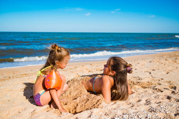 The younger sister plays with her sister by the sea.