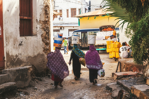 Zanzibar, Tanzania - February 21, 2019: three local woman walking in Streets of Zanzibar carrying buckets on their heads