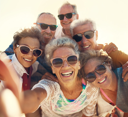 Cropped shot of a group of senior friends taking selfies while enjoying their day out on the beach