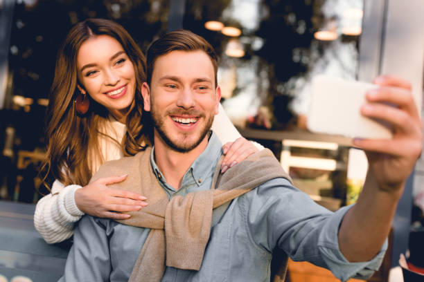 istock selective focus of cheerful man taking selfie with happy girlfriend 1149759820