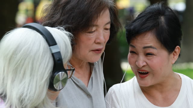 Senior Taiwanese Ladies Sharing Headphones While Listening To Music