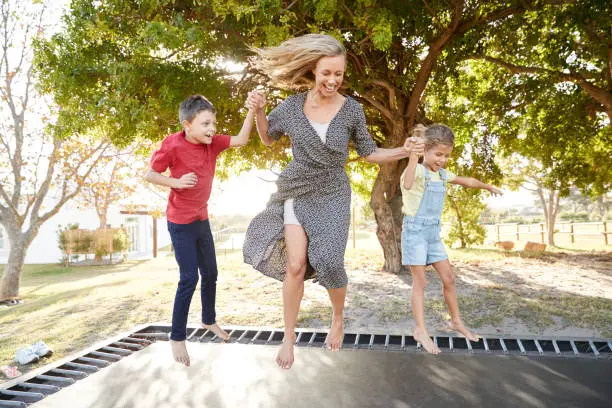 Mother Playing With Children On Outdoor Trampoline In Garden