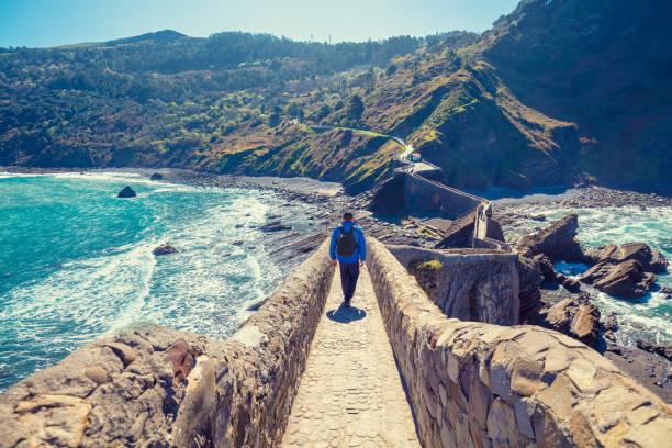 un uomo cammina sul ponte per l'isola di gaztelugatxe. baia di biscaglia, paesi baschi, spagna, europa - mountain looking at view beach cliff foto e immagini stock