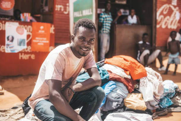 at the textile market in Mzuzu Mzuzu, Malawi - February 27, 2019: young man sitting in front of textiles stack at market in Mzuzu, Malawi malawi stock pictures, royalty-free photos & images