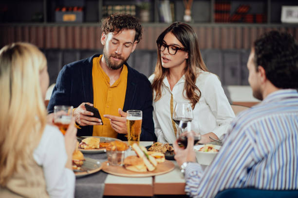 istock Couple looking at smart phone while sitting at restaurant with their friends. 1149766131