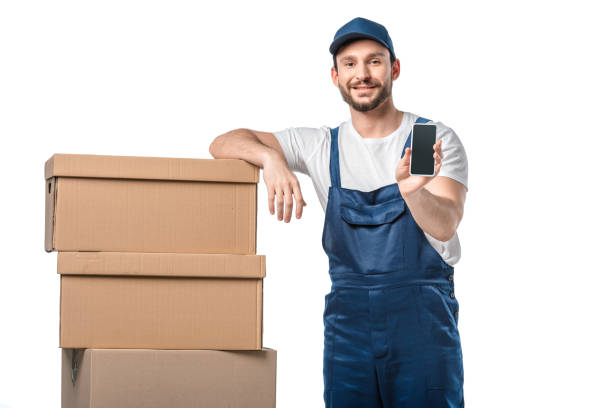 istock handsome smiling mover with cardboard boxes presenting smartphone with blank screen isolated on white 1149766548