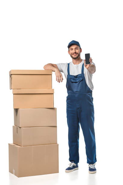 istock handsome smiling mover with cardboard boxes presenting smartphone with blank screen isolated on white 1149766551
