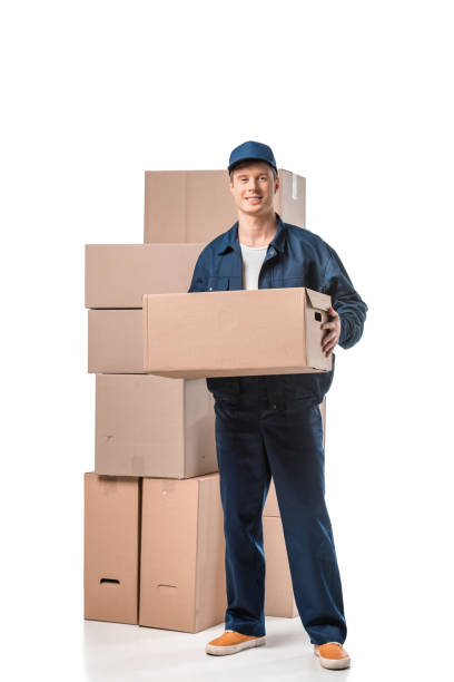 istock handsome mover in uniform carrying cardboard box and looking at camera isolated on white 1149766637