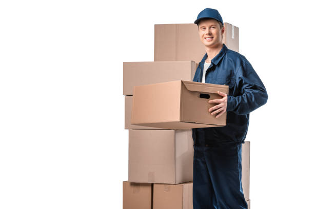 istock handsome mover in uniform carrying cardboard box and looking at camera isolated on white with copy space 1149766649