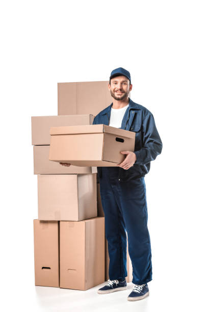istock handsome mover in uniform carrying cardboard box, smiling and looking at camera isolated on white 1149766660