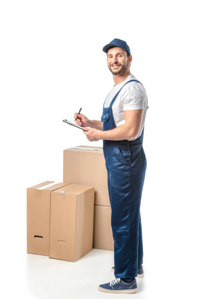 istock smiling mover in uniform writing in clipboard near cardboard boxes isolated on white 1149766669