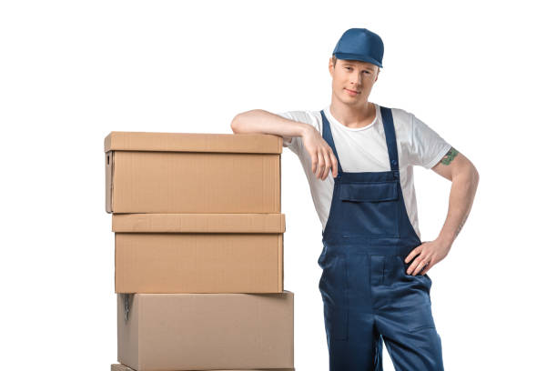 istock handsome mover in uniform with cardboard boxes looking at camera isolated on white 1149769012