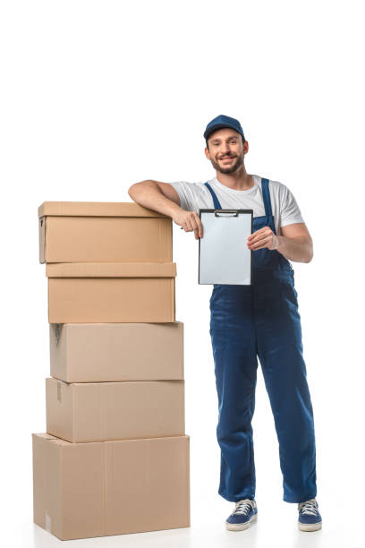 istock handsome mover in uniform looking at camera while holding blank clipboard near cardboard boxes isolated on white 1149769027