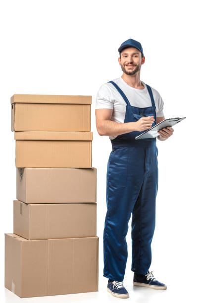 istock mover in uniform looking at camera while writing in clipboard near cardboard boxes isolated on white 1149769032