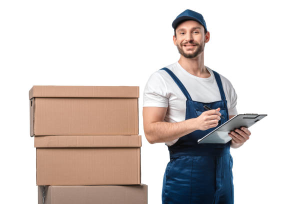 istock mover in uniform looking at camera while writing in clipboard near cardboard boxes isolated on white 1149769035
